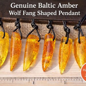 May include: Six genuine Baltic amber wolf fang shaped pendants with black cords. The pendants are a translucent yellow-orange color. The text "Genuine Baltic Amber Wolf Fang Shaped Pendant" is at the top of the image. A "Handmade Jewelry" sticker is in the bottom right corner.