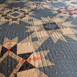 May include: A detailed quilt in shades of blue, cream, and pink, featuring geometric star and diamond patterns. The quilt has intricate stitching and a variety of fabric textures, creating a cozy and handcrafted aesthetic.