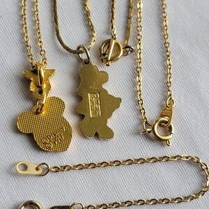 May include: Two gold-toned metal necklaces featuring character-shaped pendants. One pendant is a textured Mickey Mouse head shape with Disney branding on the back, and the other is a full-body character silhouette with a Disney China stamp on the back.