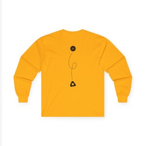 May include: Mustard yellow long-sleeve shirt with a black button and a dotted line design. The design includes a black triangle shape at the bottom. The shirt has a crew neck and long sleeves.