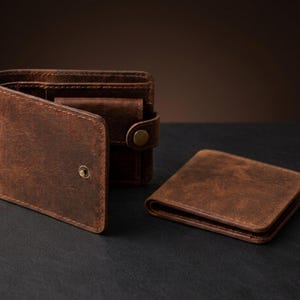 Peut inclure: Trois portefeuilles en cuir marron sont présentés sur une surface sombre. Un portefeuille est ouvert, révélant des compartiments intérieurs. Un autre portefeuille est fermé, et un troisième est en arrière-plan. Les portefeuilles ont un aspect usé et texturé.