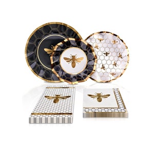 May include: A set of black and white paper plates and napkins with a gold honeycomb and bee design. The plates have a scalloped edge and the napkins are folded in a stack.