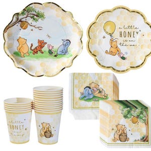 May include: A set of Winnie the Pooh themed party supplies. Includes plates, cups, and napkins with illustrations of Pooh, Tigger, Piglet, and Eeyore. The plates have a scalloped edge with gold trim. The cups and plates have the text "A little honey is on the way."
