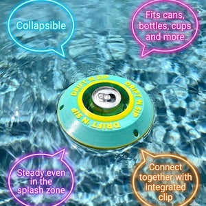 Puede incluir: Un portavasos flotante turquesa y amarillo con el texto "DRIFT N SIP" y una lata dentro. El soporte es plegable y se conecta con un clip integrado. Se adapta a latas, botellas, tazas y más, y es estable en la zona de salpicaduras.