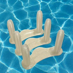 May include: Several off-white, plastic pool float connectors are arranged against a backdrop of rippling blue water. Each connector has a curved base with three vertical, cylindrical posts.