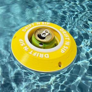 Könnte beinhalten: Ein gelb-weißer schwimmender Getränkehalter mit dem Text "DRIFT 'N SIP" in weißen Buchstaben. Eine grüne Getränkedose befindet sich im Halter, der in einem Pool mit blauem Wasser schwimmt.