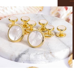 May include: A set of gold-toned cufflinks and studs with a mother-of-pearl inlay. The cufflinks are oval-shaped, while the studs are round. The text at the bottom reads: "1 Pair Cufflink + 6 Pieces Studs."
