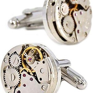 May include: A pair of silver cufflinks featuring the intricate internal mechanisms of a watch. The cufflinks showcase gears, jewels, and other components, offering a unique and mechanical aesthetic. The design includes silver-toned metal and small screws.