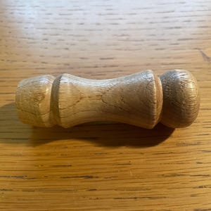 Könnte beinhalten: Ein hölzerner Flaschenverschluss mit abgerundeter Oberseite und zylindrischem Körper. Der Verschluss ist aus hellfarbenem Holz gefertigt und hat eine glatte, polierte Oberfläche. Der Verschluss ist für den Flaschenhals konzipiert.