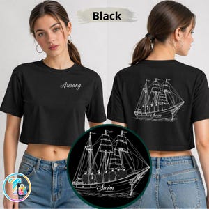 May include: Black cropped t-shirt with the word "Arirang" in white script on the front. The back features a white line drawing of a sailboat with the word "Swim" below. The shirt is worn with blue jeans.