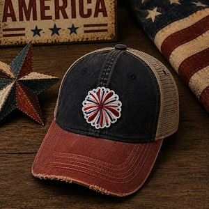 May include: A distressed baseball cap with a red brim, navy blue crown, and tan mesh back. The cap features a patriotic emblem and is set against a backdrop with an American flag and a sign that reads "GOD BLESS AMERICA."