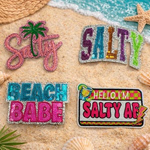 May include: Four sequined patches with beach-themed text on sand. One patch says "Salty" with a palm tree, another says "Salty" in purple, teal, and green. The third says "Beach Babe" in teal and pink, and the last says "Hello I'm Salty AF".