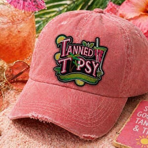 May include: A distressed, faded red baseball cap with the words "Tanned Tipsy" in a colorful patch. The cap has a curved brim and a worn appearance. The image also includes a cocktail, sunglasses, and a small sign.