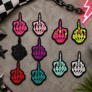 May include: A collection of ten embroidered patches shaped like skeleton hands making a middle finger gesture. The patches feature various colors including hot pink, light pink, black, purple, red, teal, neon green, and white, all with black borders.