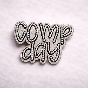 May include: A white ceramic mug with a black handle and the text "But First, Coffee" in a black, handwritten-style font. The mug is on a white surface.