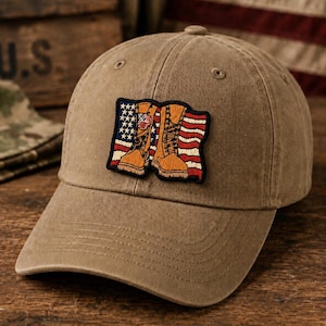May include: A khaki baseball cap with a curved brim. The cap features a patch with an American flag design and two tan combat boots. The hat is made of a durable fabric and has a classic, casual style.