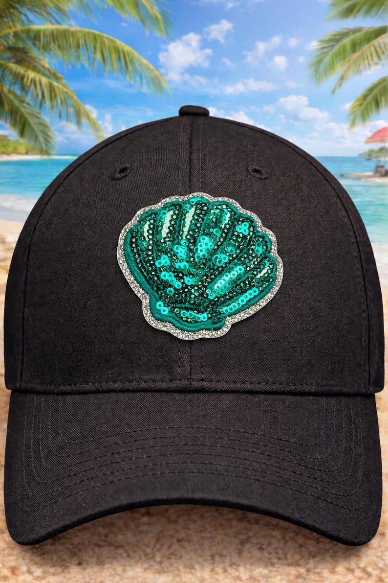 May include: Black baseball cap featuring a teal sequined seashell design, edged with silver rhinestones. The cap has a curved peak and adjustable strap. The background shows a beach scene with palm trees and blue skies.