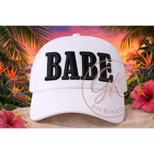 May include: White baseball cap with the word "BABE" embroidered in bold black letters. The cap is set against a tropical background with palm trees, flowers, and a sunset.
