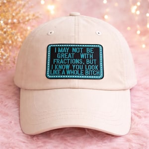 May include: A beige baseball cap with a curved brim and a button on top. The cap features a rectangular patch with the text "I MAY NOT BE GREAT WITH FRACTIONS, BUT I KNOW YOU LOOK LIKE A WHOLE BITCH" in white letters.