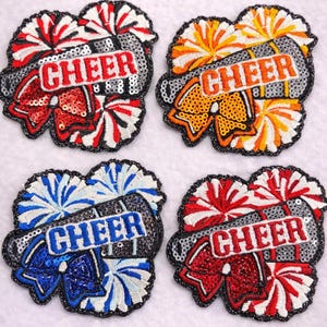May include: Four embroidered cheerleading patches. Each patch features the word "CHEER" in a sequined frame, with pom-pom and bow details in red, orange, blue, and red. The patches are on a white background.