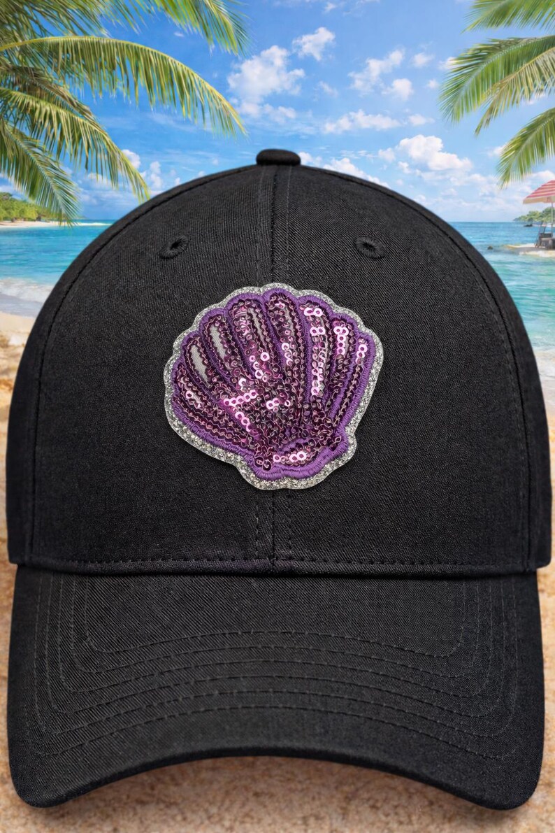 May include: Black baseball cap with a seashell motif. The shell is decorated with purple sequins and a silver glitter border. The cap has a traditional six-panel construction and a curved peak.