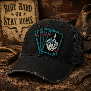 May include: Black trucker hat with a distressed brim and mesh back. The hat features a patch with playing card designs and a skeleton hand giving the middle finger. The text on the patch reads "FUCK". A wooden sign with the text "RIDE HARD OR STAY HOME" is in the background.