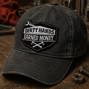 May include: A distressed black baseball cap with a patch that reads "DIRTY HANDS EARNED MONEY." The patch features a wrench, crossed hammers, and a brown border. The cap has a curved brim and a worn appearance.