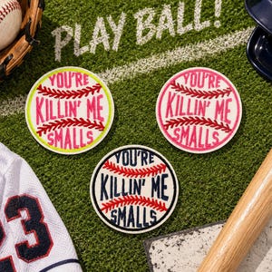 May include: Three circular embroidered patches shaped like baseballs, each featuring red stitching and the text "YOU'RE KILLIN' ME SMALLS" in the center. One patch has neon yellow borders, one has pink borders, and one has dark blue borders.