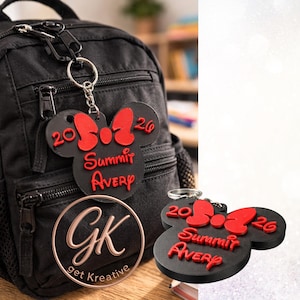 May include: Black Minnie Mouse-shaped keychain with a red bow and text. The keychain reads "20 26 Summit Avery" in red. The keychain is attached to a black backpack. A clear circular tag with "GK get Kreative" is also visible.