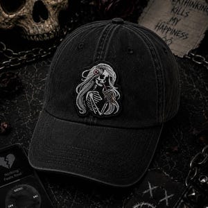 Pu&ograve; includere: Cappellino da baseball nero con una toppa raffigurante uno scheletro con lunghi capelli che tiene una bevanda. Il cappellino ha una visiera curva e un aspetto invecchiato. Il testo "Overthinking Kills My Happiness" &egrave; visibile.