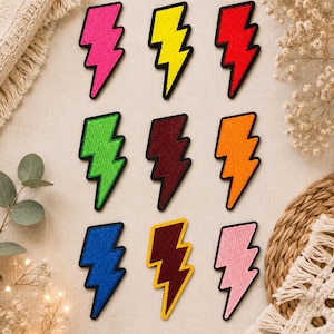 May include: Nine embroidered lightning bolt patches arranged in a grid. The colors include hot pink, neon yellow, red, lime green, dark maroon, orange, royal blue, mustard yellow, and light pink. Each patch features a thick black stitched border.