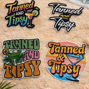 May include: Four embroidered patches with the text "Tanned and Tipsy" in various designs. One patch features a cocktail, another a margarita, and a third a cocktail against a sunset background. The patches are on a sandy beach with seashells.