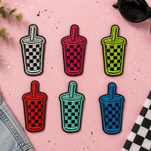 May include: Six embroidered patches shaped like cups with straws, each featuring a checkered pattern. The colors include white and black, pink and black, lime green and black, red and black, teal and black, and blue and black, all with black borders.