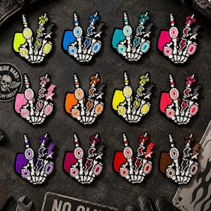 May include: A collection of twelve embroidered patches, each featuring a white skeleton hand making a peace sign. The hand is adorned with colorful rings, flowers, stars, and lightning bolt shapes, with a solid colored background behind each hand.