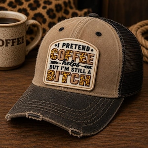 May include: A distressed brown and black trucker hat with a mesh back. The hat features a patch with the text "I PRETEND. COFFEE helps BUT I'M STILL A BITCH" in a mix of fonts and leopard print accents. The hat has a curved brim.