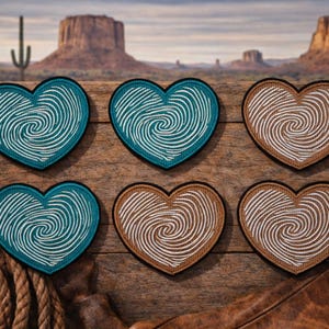May include: Six heart-shaped patches with fingerprint designs. Three are teal with white prints, and three are brown with white prints. The patches are on a wooden surface with a desert landscape background.