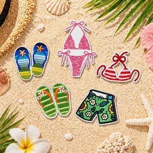 May include: A collection of embroidered beach-themed patches, including a pink bikini, striped bikini top, and green swim trunks with floral designs. Also featured are flip-flops and a straw hat, all arranged on a sandy surface with tropical elements.
