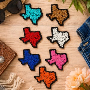May include: A collection of embroidered patches in the shape of the state of Texas, each featuring a floral design. The patches come in various colors, including turquoise, brown, red, white, blue, pink, and orange, with a black border.