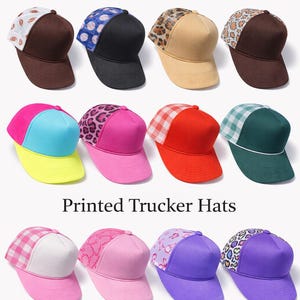 May include: Assortment of printed trucker hats in various colors and patterns. Designs include leopard print, gingham, and floral patterns. The hats have mesh backs and curved brims. The text "Printed Trucker Hats" is displayed.