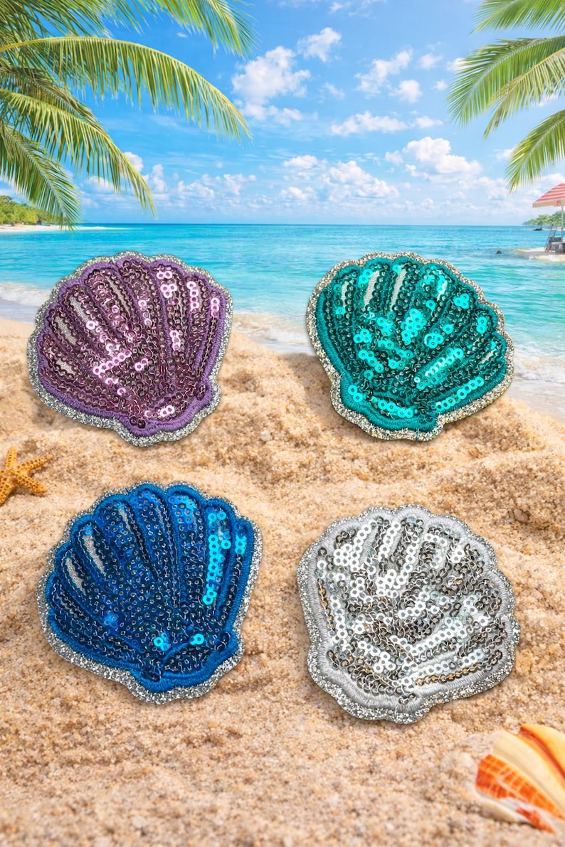 May include: Four sequined seashell patches in purple, teal, blue, and silver, with silver trim. The patches are arranged on a sandy beach with a blue ocean and sky in the background. Palm trees and a beach umbrella are visible.