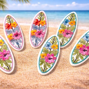 May include: Six surfboard-shaped embroidered patches with colorful floral designs. Each patch features a white background, a colorful floral arrangement, and a contrasting border. The patches are arranged on a sandy surface with a beach and ocean background.
