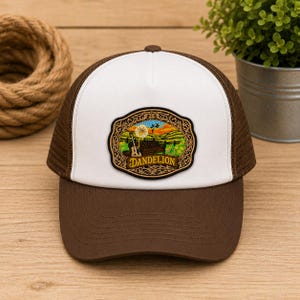 May include: A brown and white trucker hat featuring a central embroidered patch. The patch displays a landscape with a dandelion, a guitar, and the word DANDELION in a decorative gold frame. The hat has a solid brown brim and mesh back.
