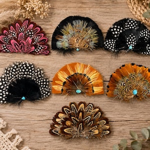 May include: Seven semi-circular feather brooches arranged in a grid. Each brooch features a unique pattern of natural feathers in shades of pink, black, white, orange, and brown, accented with a small, round, light blue turquoise-colored stone.