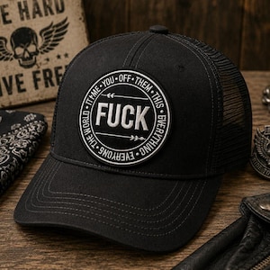 May include: Black trucker hat with a mesh back and a curved brim. The hat features a circular patch with the word "FUCK" in bold white letters. The patch is surrounded by text that reads "THE WORLD - TTM - YOU OFF - THEM - THIS - EVERYTHING - EVERYONE".