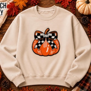 May include: A beige crewneck sweatshirt featuring a central graphic of an orange pumpkin adorned with a black and white checkered bow. The text PATCH ONLY is printed in the upper left corner in a bold, black, sans-serif font.