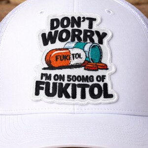 May include: White trucker hat with a mesh back and a curved brim. The front patch features the text "DON'T WORRY I'M ON 500MG OF FUKITOL" with a pill graphic in orange, teal, and white.