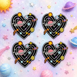 May include: Four identical heart-shaped patches featuring a black background with white concentric heart-shaped lines. Each patch displays embroidered celestial elements including a pink planet with rings, a yellow sun, a yellow striped planet, and stars.