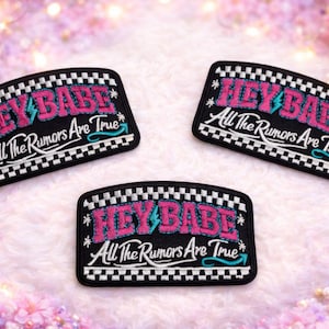 May include: Three black patches with the text "HEY BABE" in pink and teal, and "All The Rumors Are True" in white. The patches have a black and white checkered border and are on a soft, pink surface.