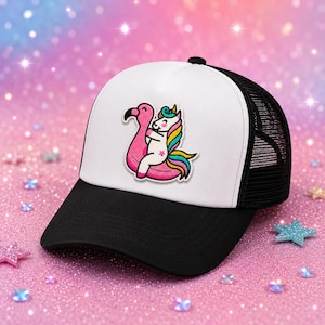 May include: A black and white trucker hat featuring a patch of a white unicorn with a multicolored mane and tail riding a pink flamingo pool float. The cap has a solid white front panel, a black brim, and a black mesh back for ventilation.