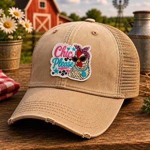 May include: Tan trucker hat with a mesh back and a distressed brim. The hat features a patch with the text "Chic Please" and a cartoon chicken wearing sunglasses and a bandana. The hat is a stylish accessory.